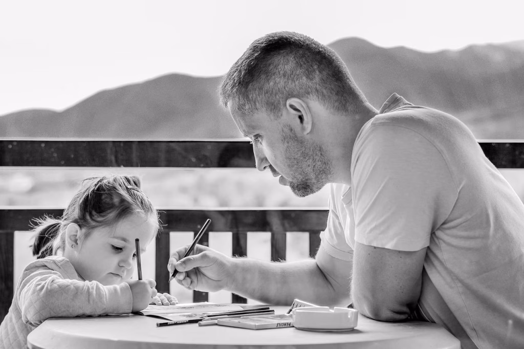 A man and his little girl are seated at a table, focused on writing, illustrating a bonding moment between father and child.
